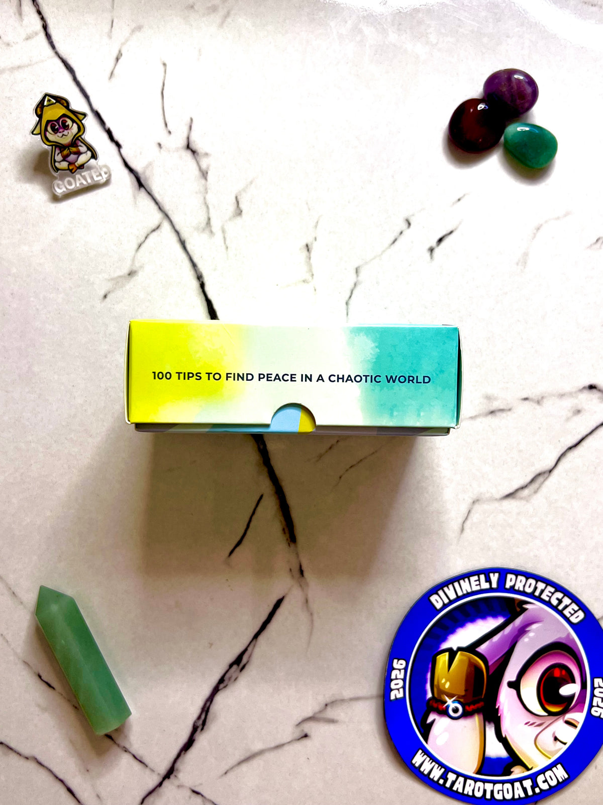 The side of meditations cards that reads 100 tips to find inner peace on a marble table with crystals and tarot goat magnet