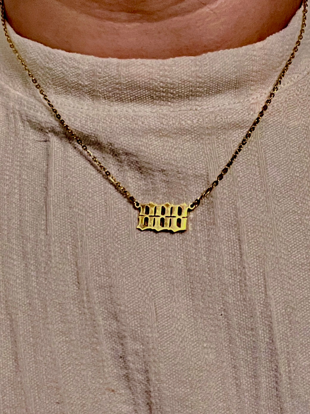 A close-up of a person wearing a gold necklace with an 888 number pendant over a light beige knit top.