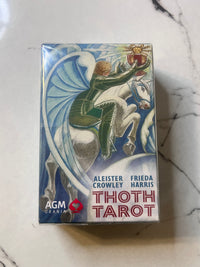 A boxed deck of Thoth Tarot cards by AGM Trania, featuring illustrated artwork of a rider on a white horse with blue wings, photographed on a light marble-like surface.