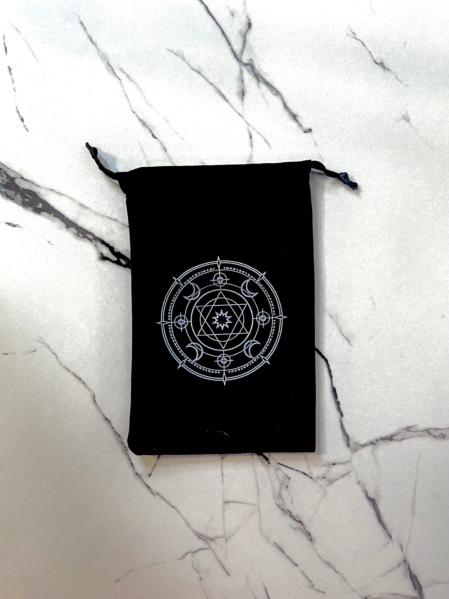 Black drawstring bag with a star witchy symbol for energy protection on a marble surface 