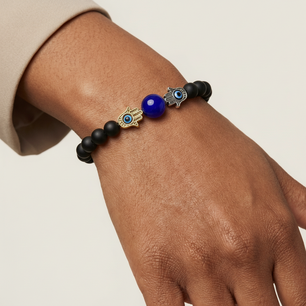 Bracelet with black beads, blue evil eye bead, and gold hand of Fatima charm on a wrist.