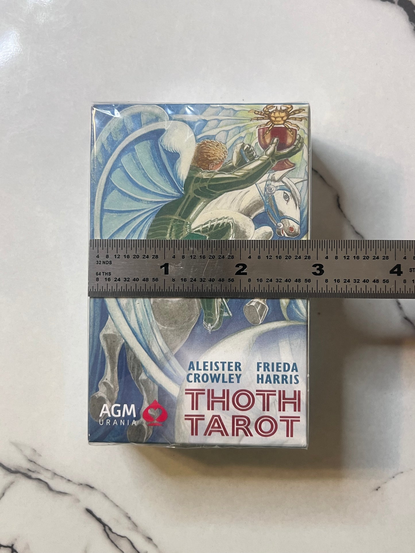AGM Thoth Tarot deck box with a ruler placed horizontally across the middle to show the deck's height, photographed on a white marble surface.