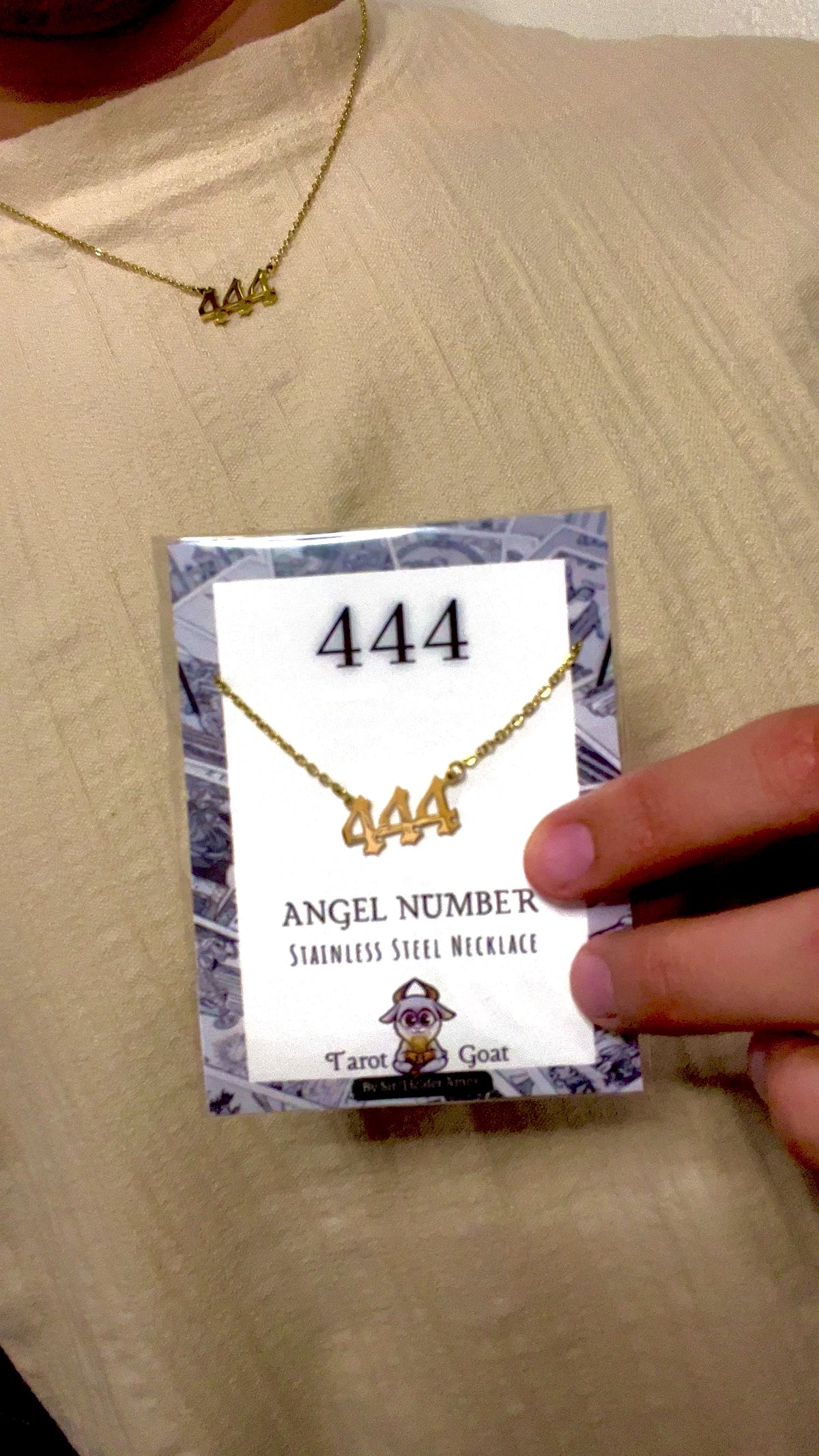 Model wearing a 444 number cecklace holding the angel number packaging with brand tarot goat for men and women 